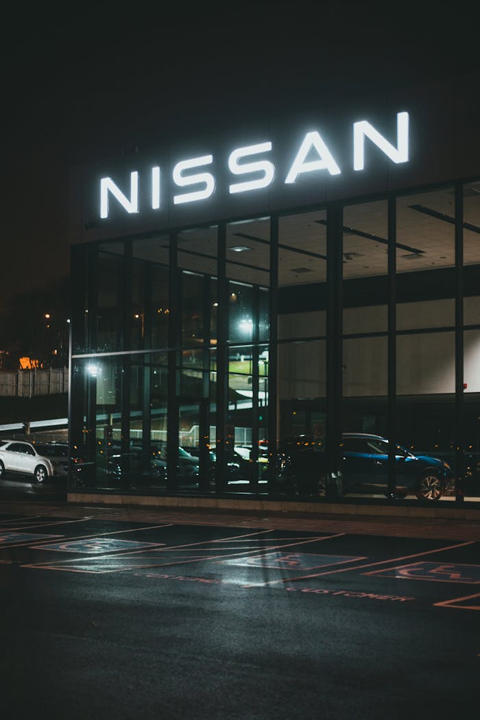 A modern car dealership with a glass facade illuminated at night, showcasing luxury vehicles.
